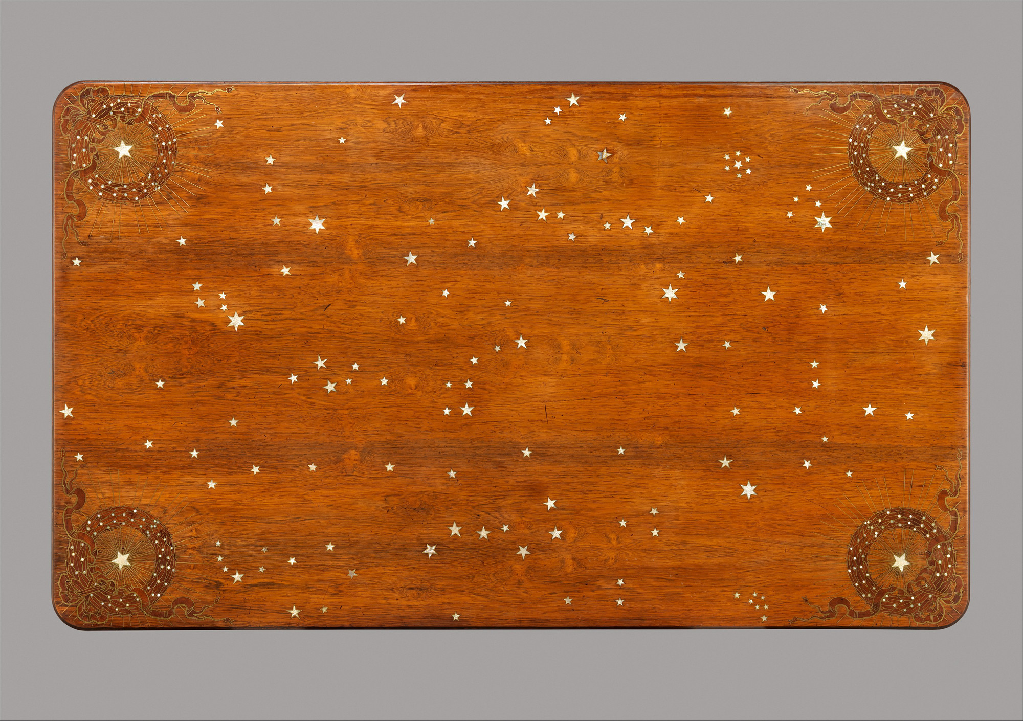 Overhead view of the library table's rosewood top scattered with shell stars and four radiating star wreaths at the corners.