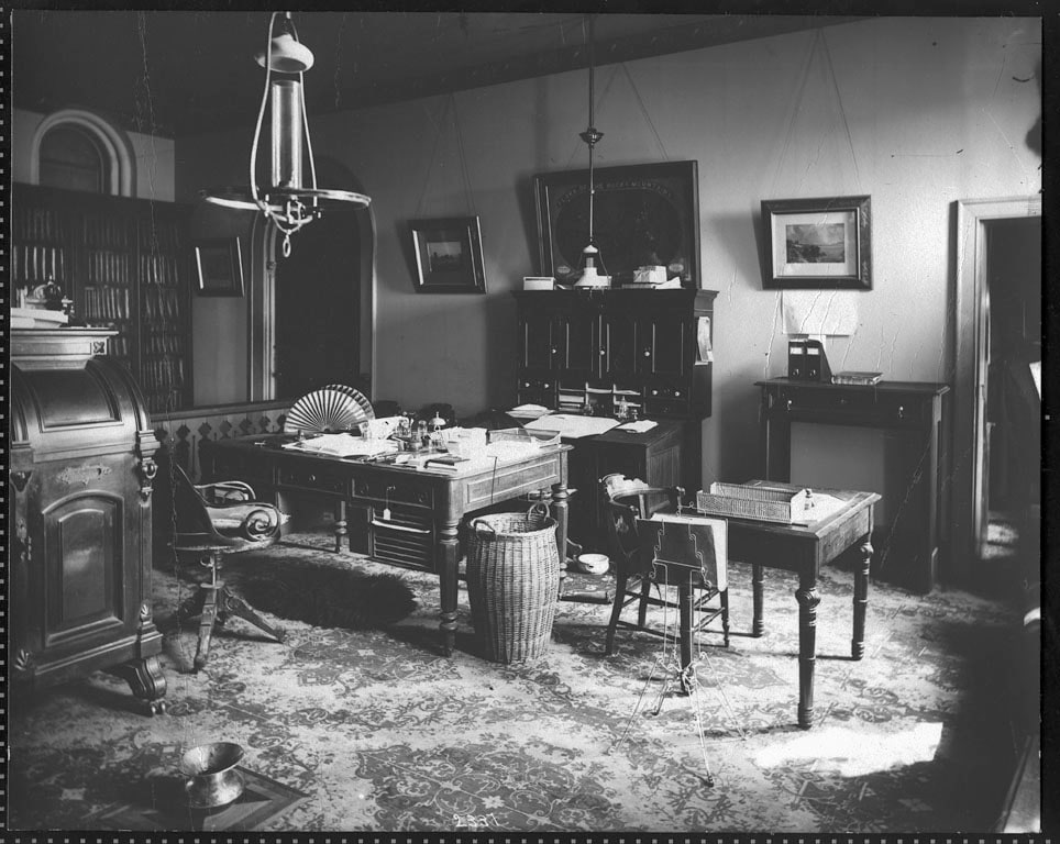 A crowded 1878 Smithsonian office with Spencer Fullerton Baird at a central table and an open Wooton secretary visible against the far-left wall.