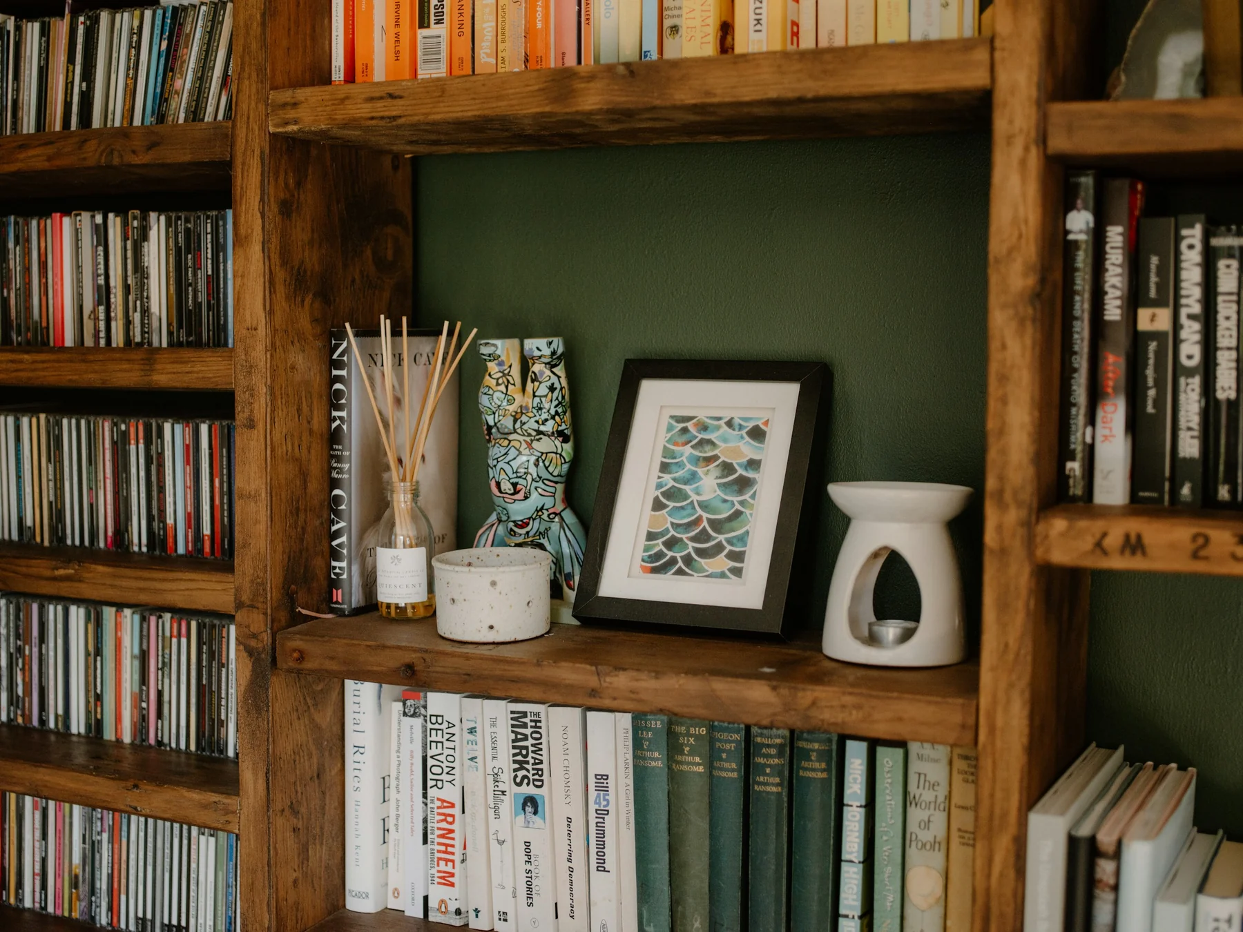 Wooden shelves with books of different heights, rows of CDs and a larger bay holding ceramics and a framed picture.