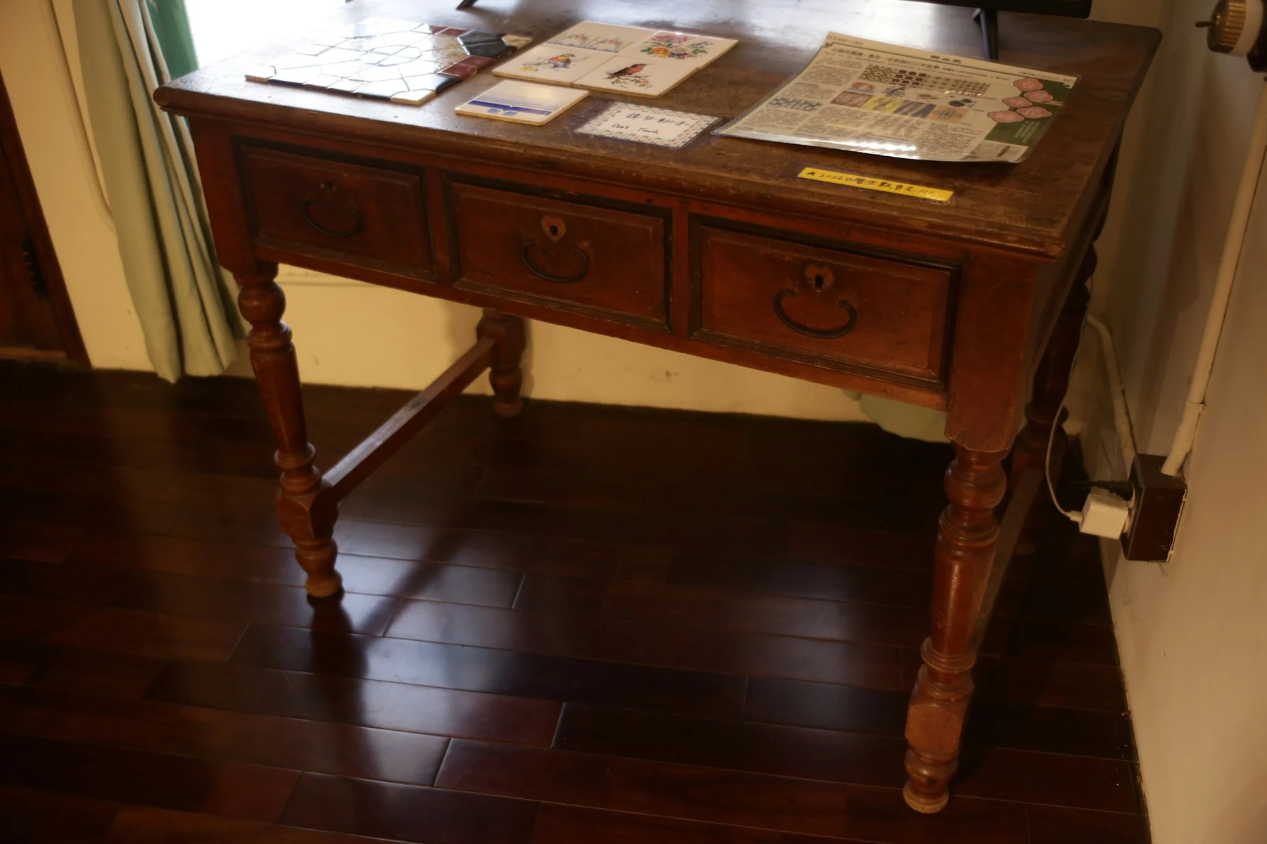 Dark wooden desk with three drawers, turned legs and a stretcher, with papers and leaflets on the top.