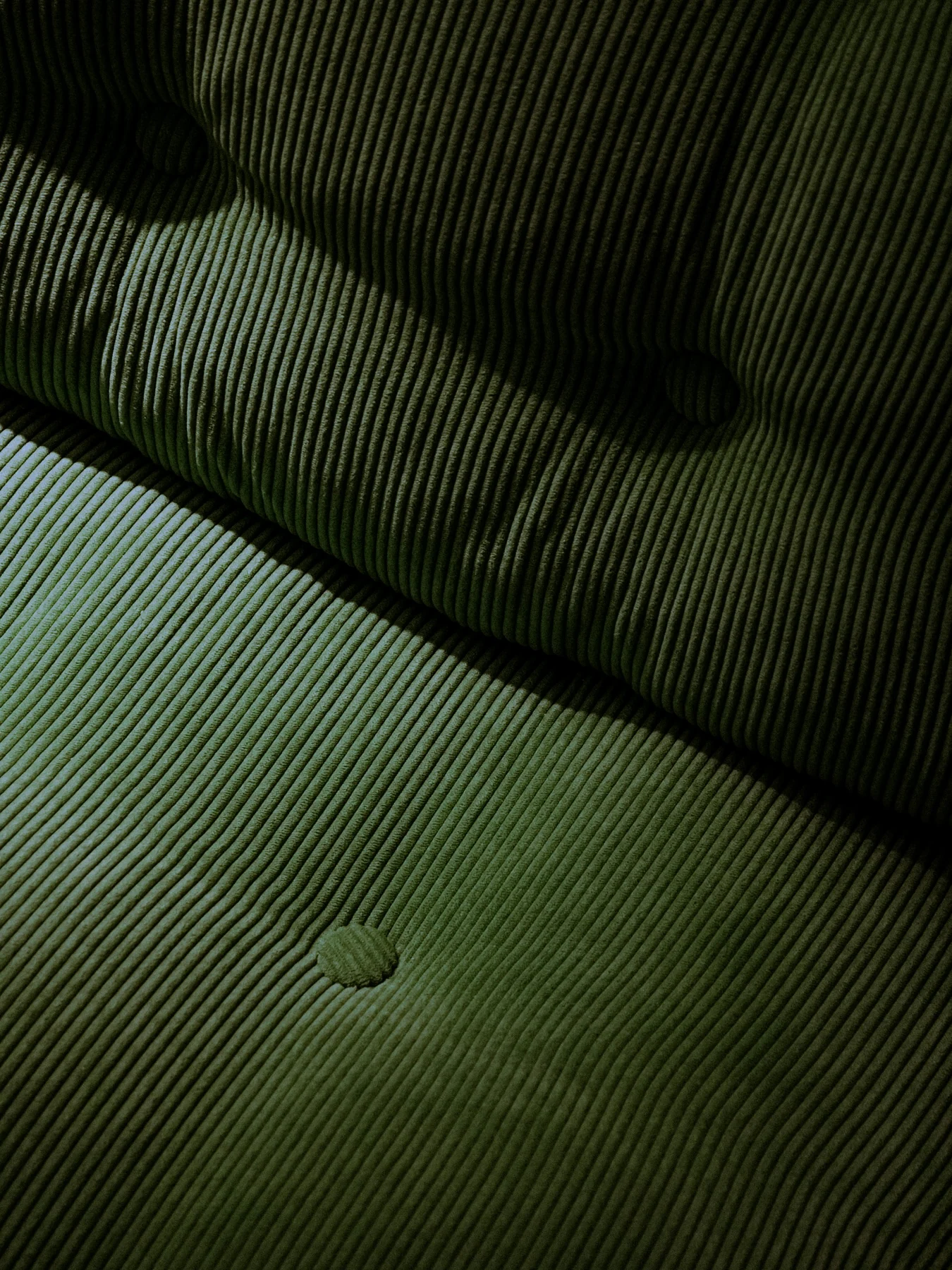 Green ribbed upholstery with covered buttons, showing light and shadow across the seat and back.
