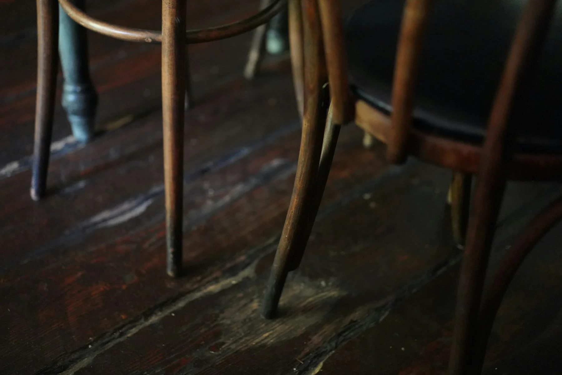 Close view of several slender wooden chair legs meeting a worn dark wooden floor.