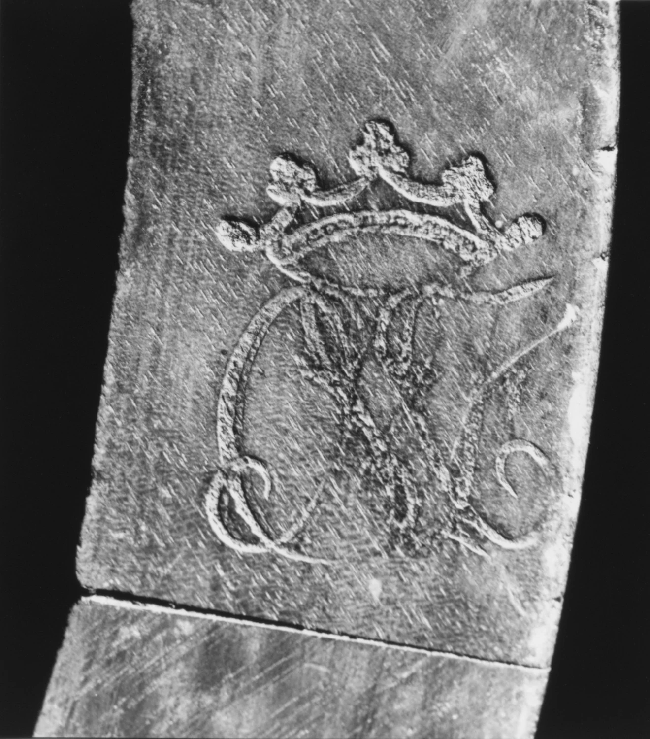 A black-and-white close view of crowned initials branded into the underside of a wooden chair rail.