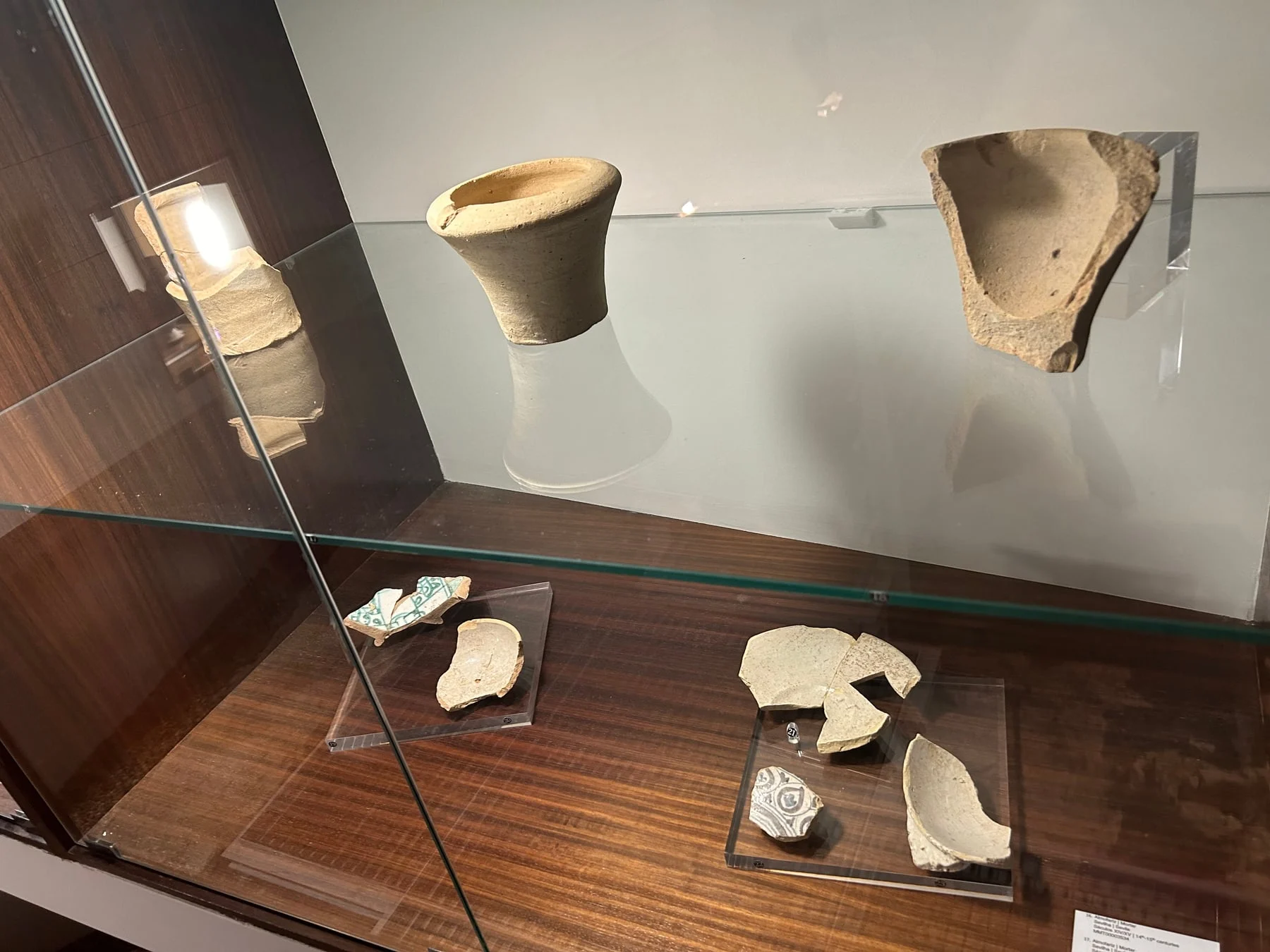 Angled close view into a glazed display case, showing the edge of a glass shelf and small fittings along its back.