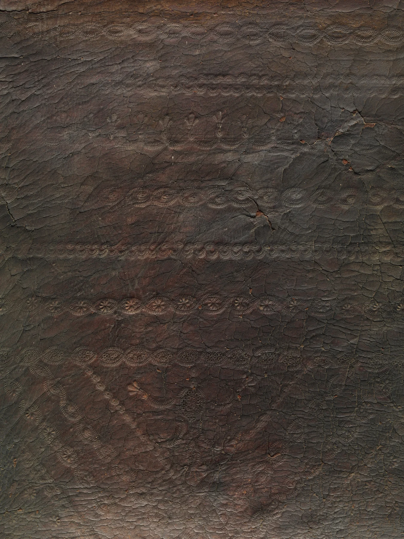 Close view of the chair's dark embossed leather showing a worn patterned field crossed by wrinkles, cracks and changes in sheen.