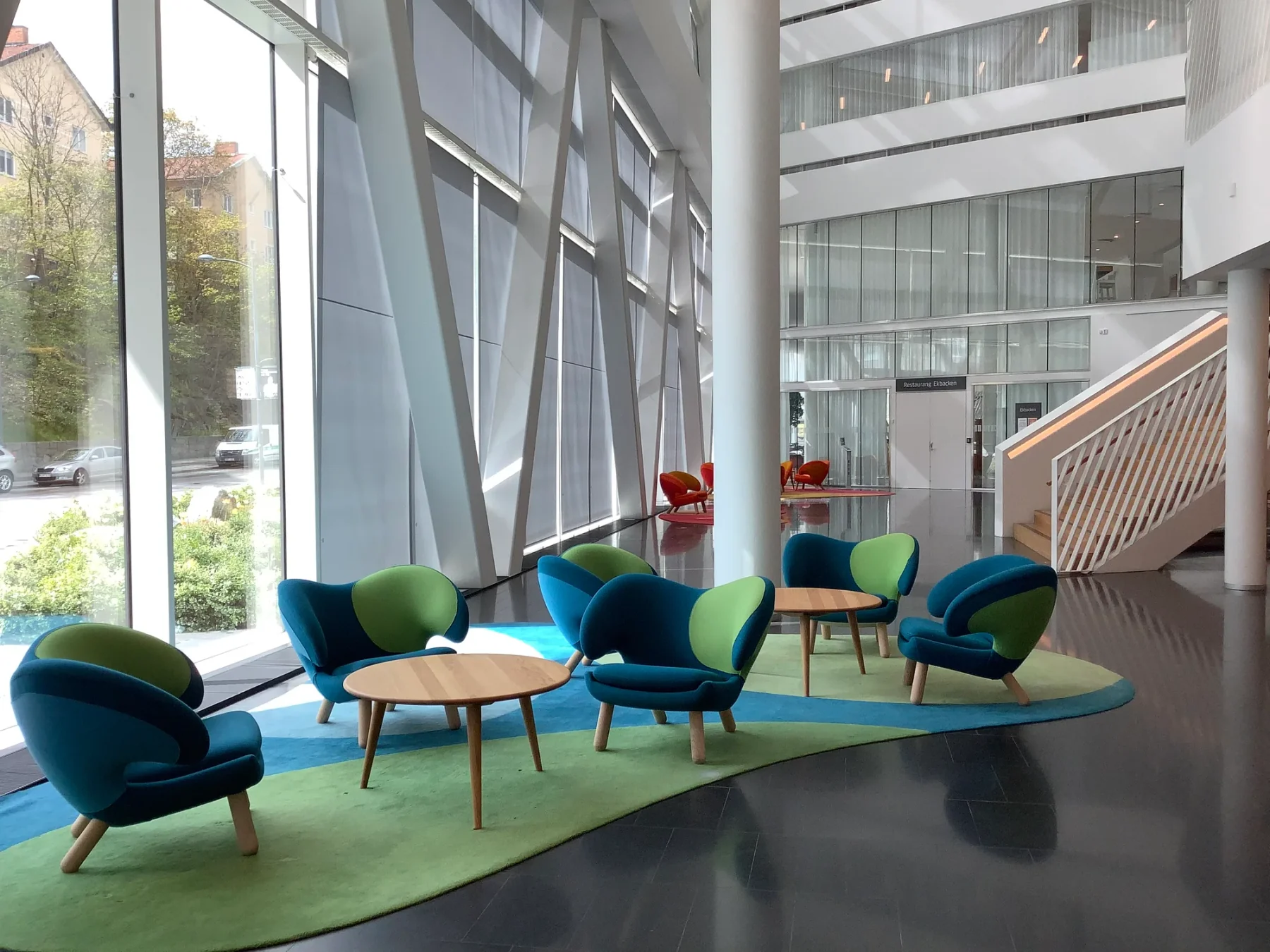 Several blue-and-green Pelican Chairs arranged in a bright lobby, seen from front, side and rear around low timber tables.