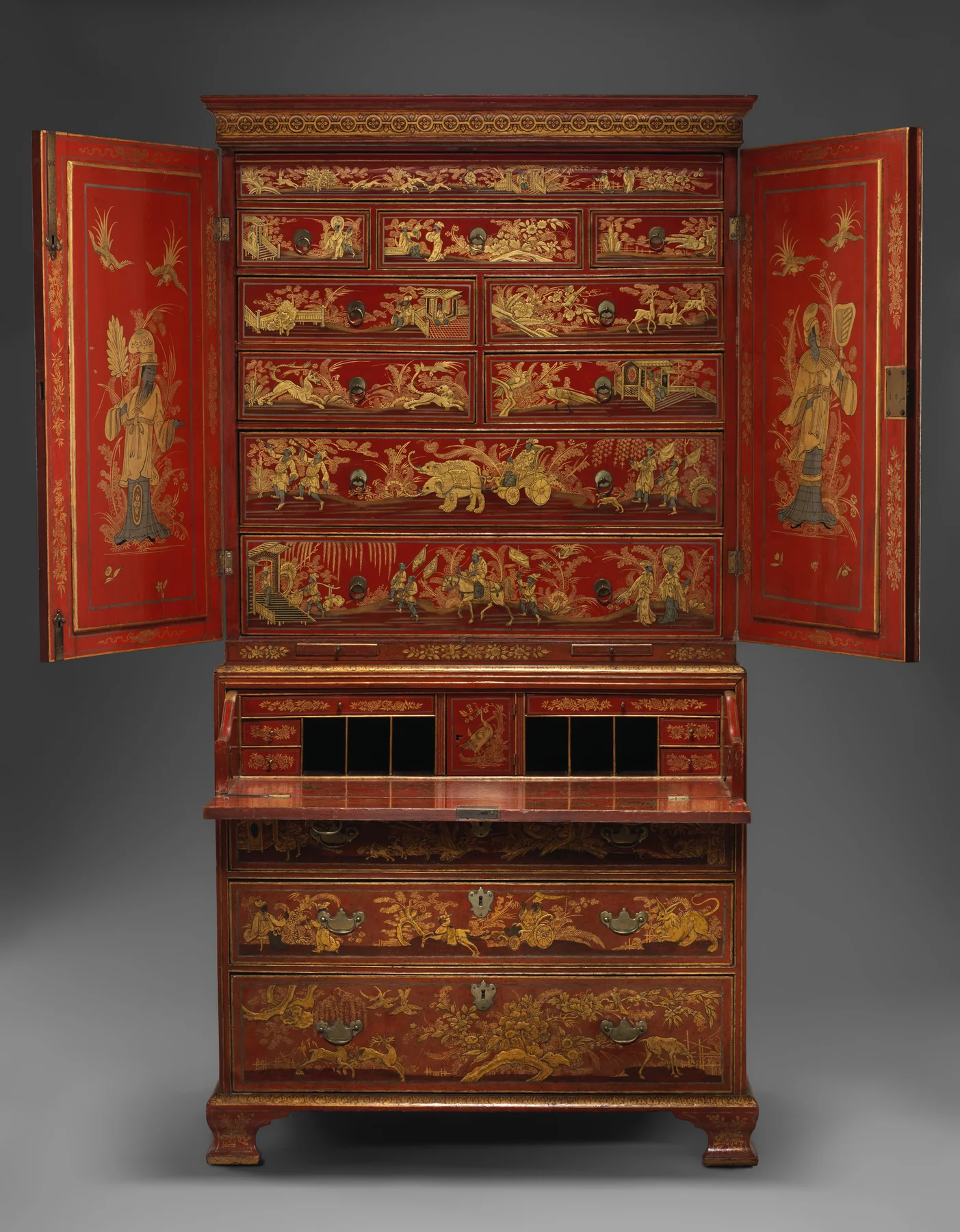 Full frontal view of a tall red japanned secretary cabinet opened to reveal painted upper drawers and a lowered writing surface.