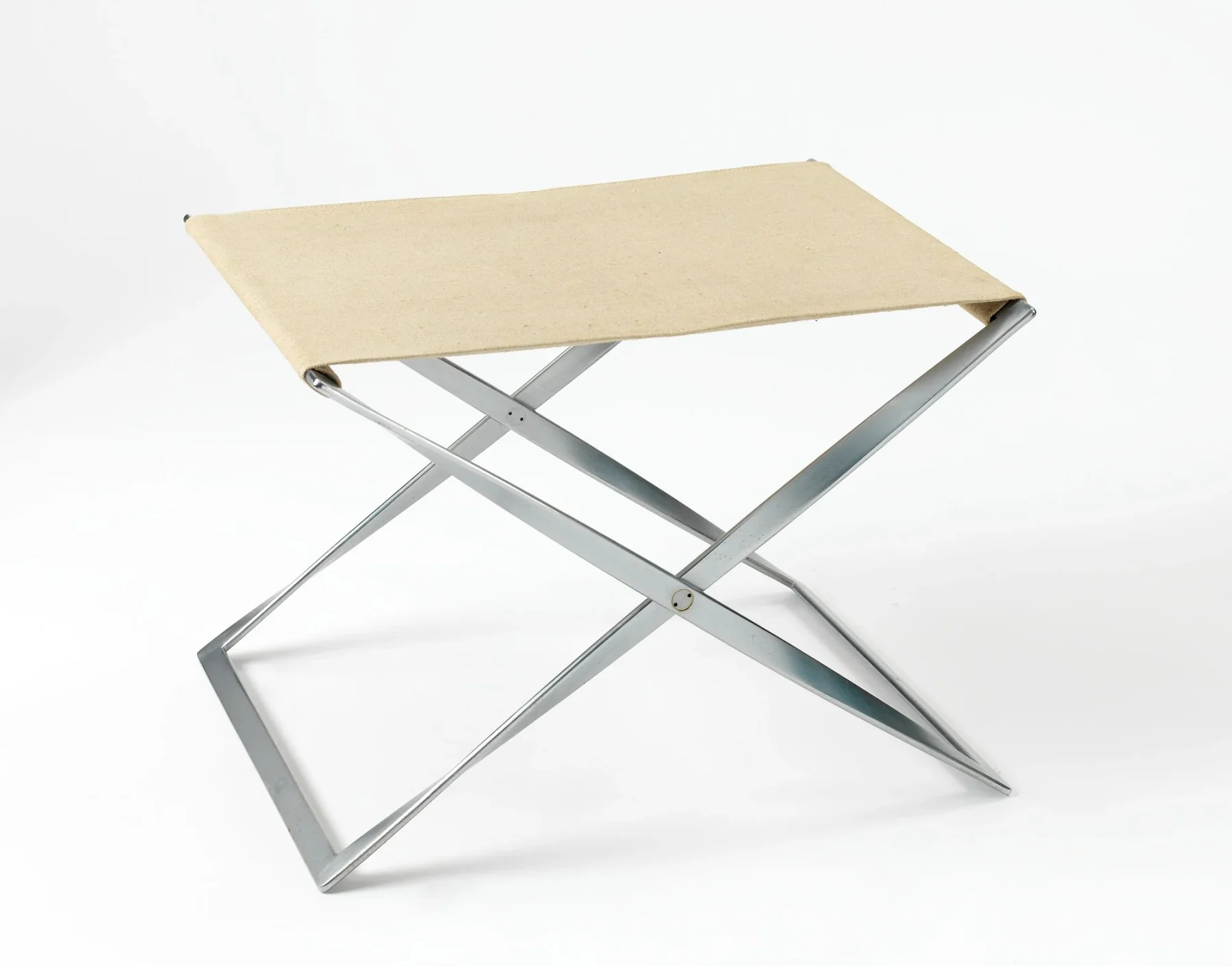 Three-quarter view of a PK91 folding stool with a pale canvas seat stretched across two crossing chrome-plated steel ribbon frames.