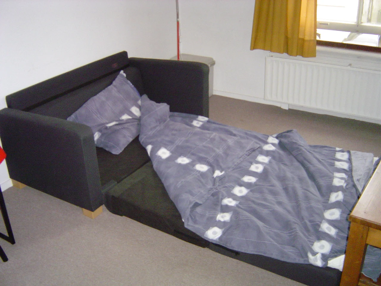 The same black sofa unfolded into a bed extending across the floor, with bedding on the open sleeping surface.