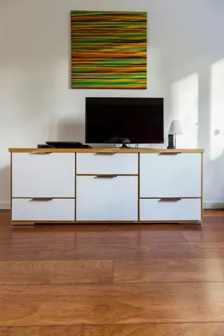 Television on a contemporary cabinet with white drawer and door fronts, a wooden top and framed art above.