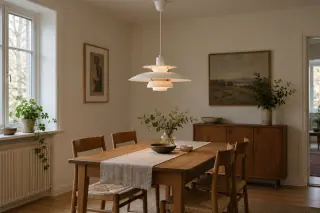 A white layered pendant hangs over a wooden dining table, with its ceiling canopy and full shade silhouette visible.
