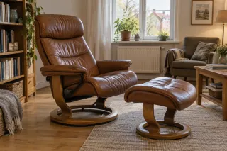 Padded brown leather reclining chair with a separate footstool and wooden ring base in a reading corner.