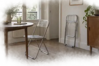 Two clear folding chairs in a dining space, one open and one folded against the wall.