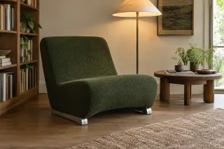 A low green upholstered chair with a continuous seat-and-back shape stands beside a small table.