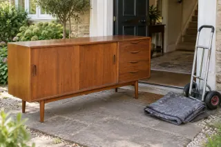 A wooden sideboard near a ground-floor doorway, with a trolley and folded moving blanket nearby.