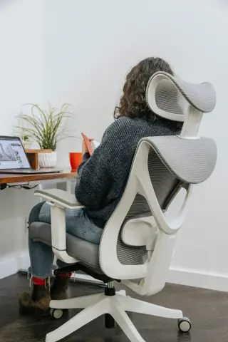 Rear three-quarter view of a person seated in a pale adjustable office chair at a desk.