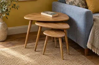 Three graduated wooden side tables partly nested beside a blue sofa.