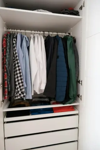 Open white PAX wardrobe with hanging shirts, shelves, a pull-out tray and drawers.