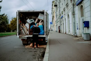 People at the open back of a furniture-filled moving truck parked beside a building.