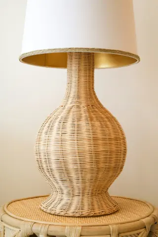 Woven lamp base with a pale tapered shade on a circular woven side table.