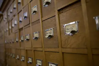 Rows of wooden card-catalogue drawers with metal pulls and paper label holders, including uneven gaps at several fronts.