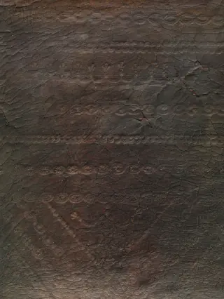 Close view of the chair's dark embossed leather showing a worn patterned field crossed by wrinkles, cracks and changes in sheen.