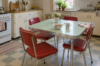 Pale green laminate-topped dining table with metal edging and red upholstered chairs in a compact kitchen.