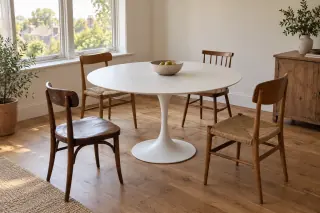 A round white pedestal dining table stands among four different vintage wooden chairs.