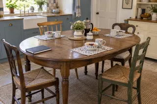 An oval wooden dining table set for breakfast with four different wooden chairs in a kitchen.