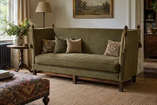 A high-sided upholstered sofa with cords and tassels in a living room.