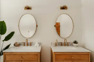 Two wooden drawer-front bathroom units with pale tops, inset basins and oval mirrors.