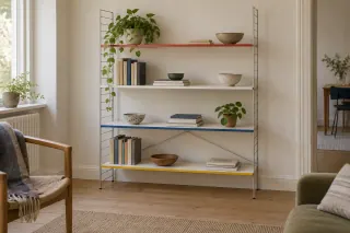 Open metal-frame shelving with coloured shelf edges and a light arrangement of books and bowls.
