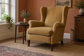 An ochre upholstered wingback chair with a loose seat cushion and exposed wooden legs in a sitting room.