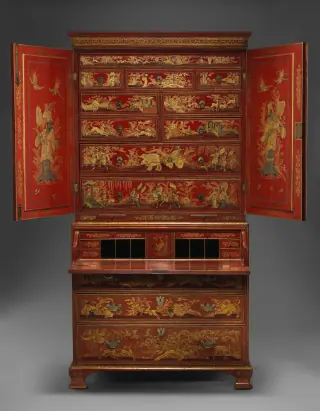 Full frontal view of a tall red japanned secretary cabinet opened to reveal painted upper drawers and a lowered writing surface.