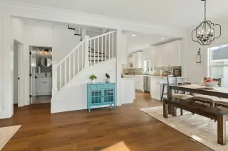 Open dining area with a wooden table and backless bench beside a kitchen and staircase.