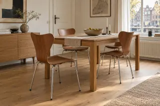 Three brown moulded-shell chairs stand around a wooden dining table in a bright apartment.