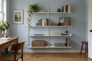 Two bays of white wall shelving hold books and a closed laptop in a small study.