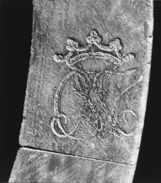 A black-and-white close view of crowned initials branded into the underside of a wooden chair rail.
