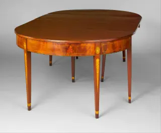 Oval wooden dining table assembled from two rounded end sections with rectangular hinged leaves, decorated aprons and tapered legs.
