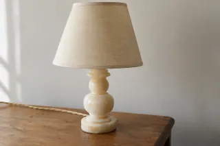 A pale turned-stone lamp base with a textile shade on a wooden table.