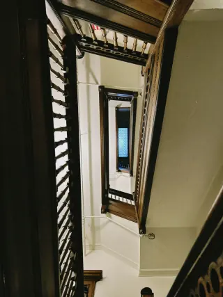 View down an old stairwell showing successive wooden landings, turns, handrails and the opening between flights.