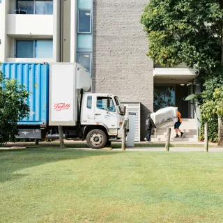 Furniture delivery truck parked beside an apartment building, with a wrapped item being carried along the approach.