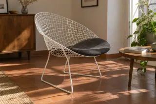 A white wire lounge chair with a dark seat pad in a sunlit room with a tiled floor.