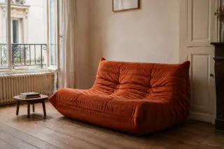 A low, pleated orange lounge sofa beside a small round table in a sitting room.