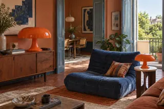 A large orange mushroom-shaped lamp on a sideboard and a smaller one beside a blue chair.