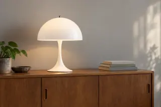 White dome-shaped table lamp with a flared base on a wooden sideboard, beside a short stack of books