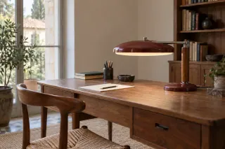 A broad red desk-lamp shade on a wooden support above a writing surface.