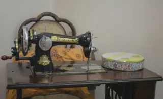 Black hand-cranked sewing machine set into a dark wooden tabletop, with the table edge and part of the frame visible.