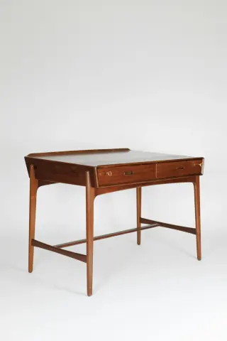 Wooden writing desk seen at an angle, with two shallow drawers, a deep apron, slim legs and low stretchers.
