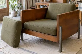 An upholstered chair with an exposed wooden case and external metal legs, with a loose cushion beside it.